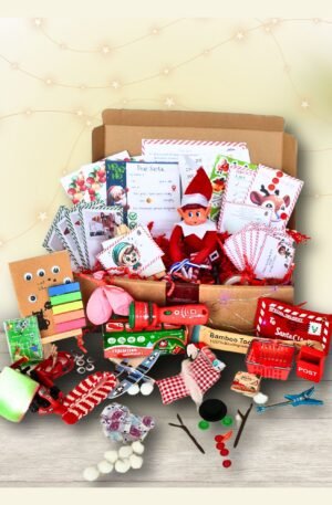 Open Elf Box with 24 days of elf props, printable notes, a Christmas elf doll, and holiday accessories arranged neatly inside. Includes red shredded paper and colourful festive items.